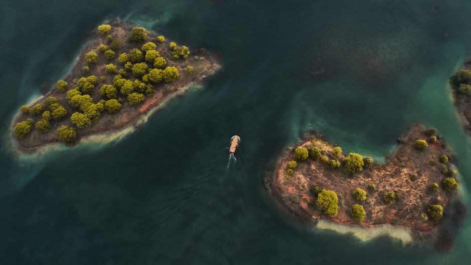 Top view of small vessel crossing rippling turquoise water of ocean between parts of land covered with green trees (photo by Sanat Anghan on Pexels)