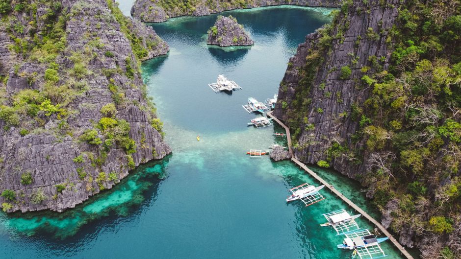 Stunning aerial shot of boats in crystal clear waters surrounded by rocky cliffs in Coron, Philippines. (photo by Jay CP on Pexels)