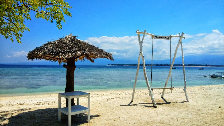 Tranquil beach scene with a swing and thatched umbrella in West Nusa Tenggara, Indonesia. (photo by timv924 on Pexels)