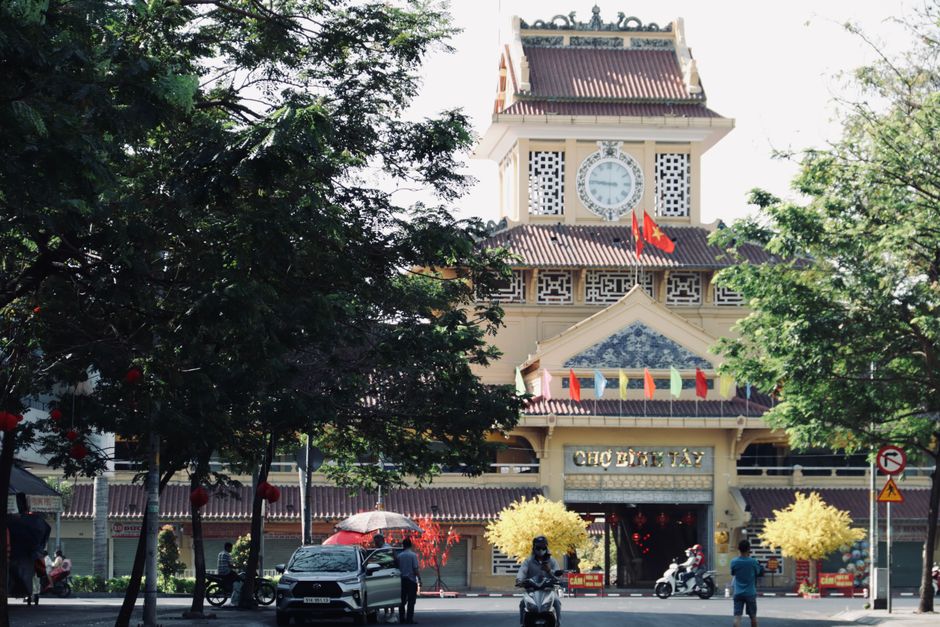 Siem Reap to Ho Chi Minh City: Bus and Flight Guide (2026) Scenic view of the iconic Binh Tay Market entrance with surrounding trees and vibrant flags in Ho Chi Minh City, Vietnam. (photo by Tuan Vy on Pexels)