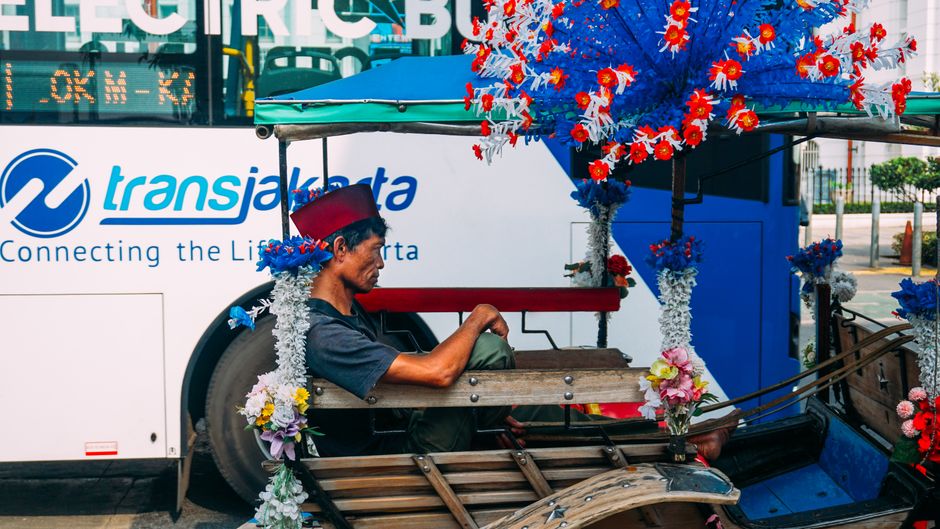 Colorful horse cart with driver in traditional attire amidst Jakarta's bustling streets, symbolizing urban culture. (photo by ridwan adee on Pexels)
