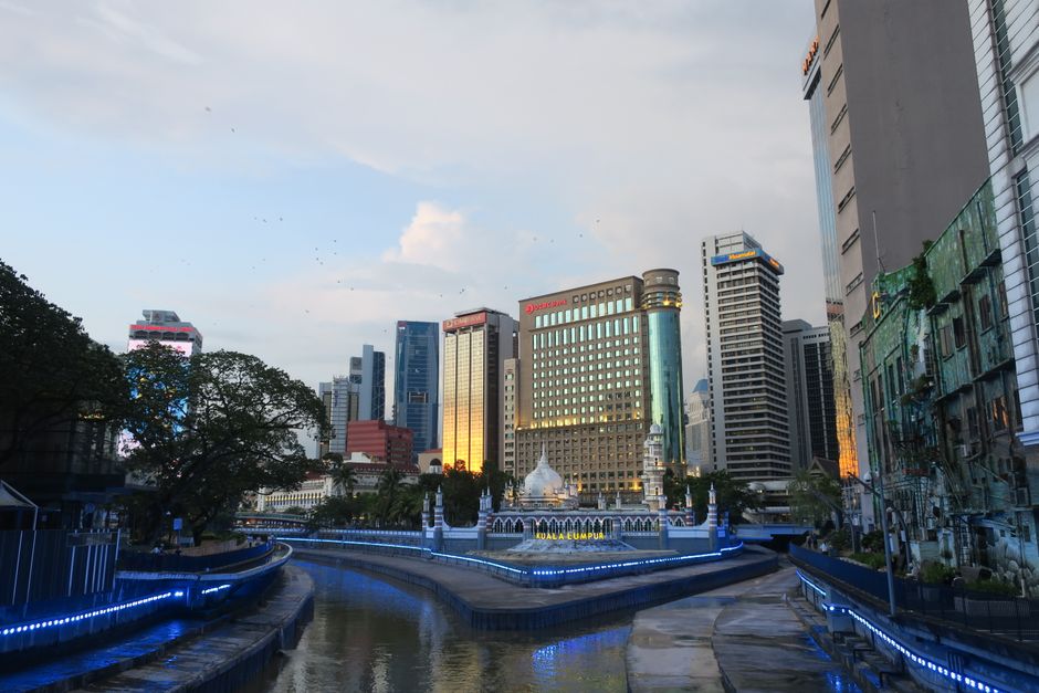 Bangkok to Kuala Lumpur: Flight, Train and Bus Guide (2026) A stunning sunset view of Kuala Lumpur's skyline with a river in the foreground, showcasing modern architecture. (photo by Mytho Digital on Pexels)
