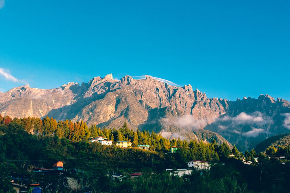 A breathtaking aerial view of Mount Kinabalu with vibrant blue skies and a charming village below. (photo by Ihsan Adityawarman on Pexels)