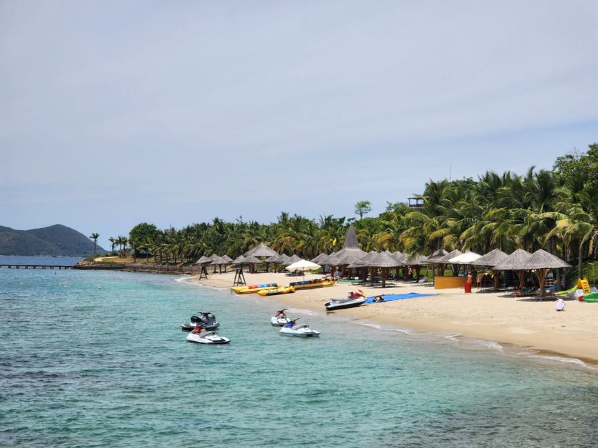 A serene tropical beach with jet skis, palm trees, and thatched umbrellas along the shoreline. (photo by Sarah Vivian on Pexels)