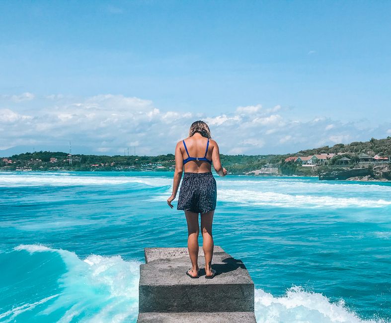 A woman stands on a pier, embracing the tropical ocean view in Bali, Indonesia. Perfect summer escape. (photo by Tiff Ng on Pexels)