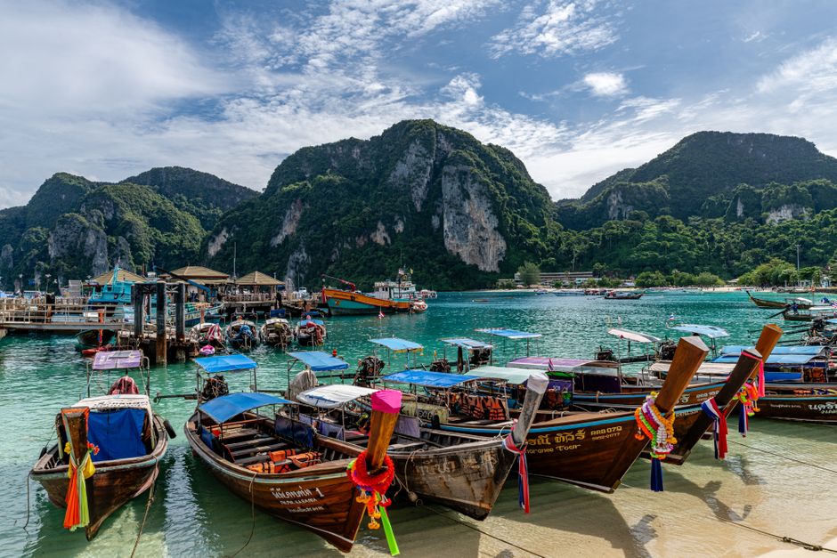 Colorful wooden boats anchored in a picturesque bay with lush hills in Phuket, Thailand. (photo by Kirandeep Singh Walia on Pexels)
