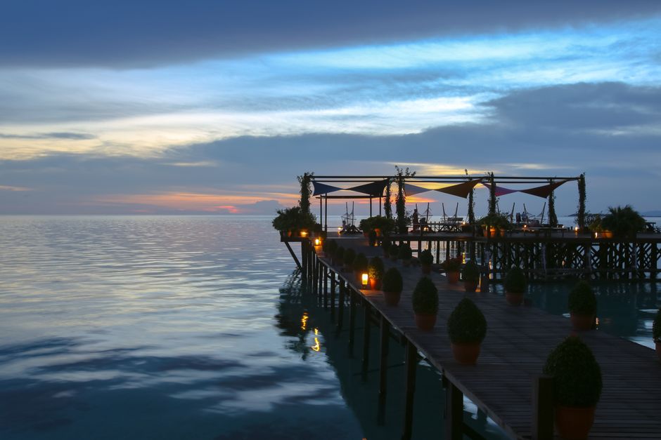 A tranquil boardwalk over the ocean at sunset with warm lighting, perfect for a tropical getaway. (photo by vitalina on Pexels)