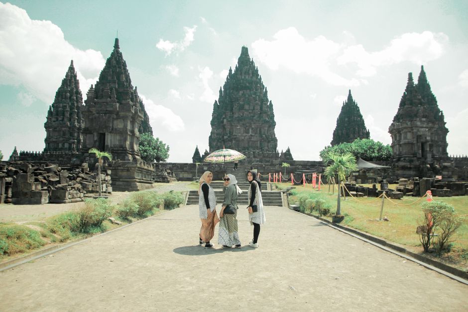 Three tourists stand with an umbrella at Prambanan Temple in Jogja, Indonesia. (photo by Bangunfii on Pexels)